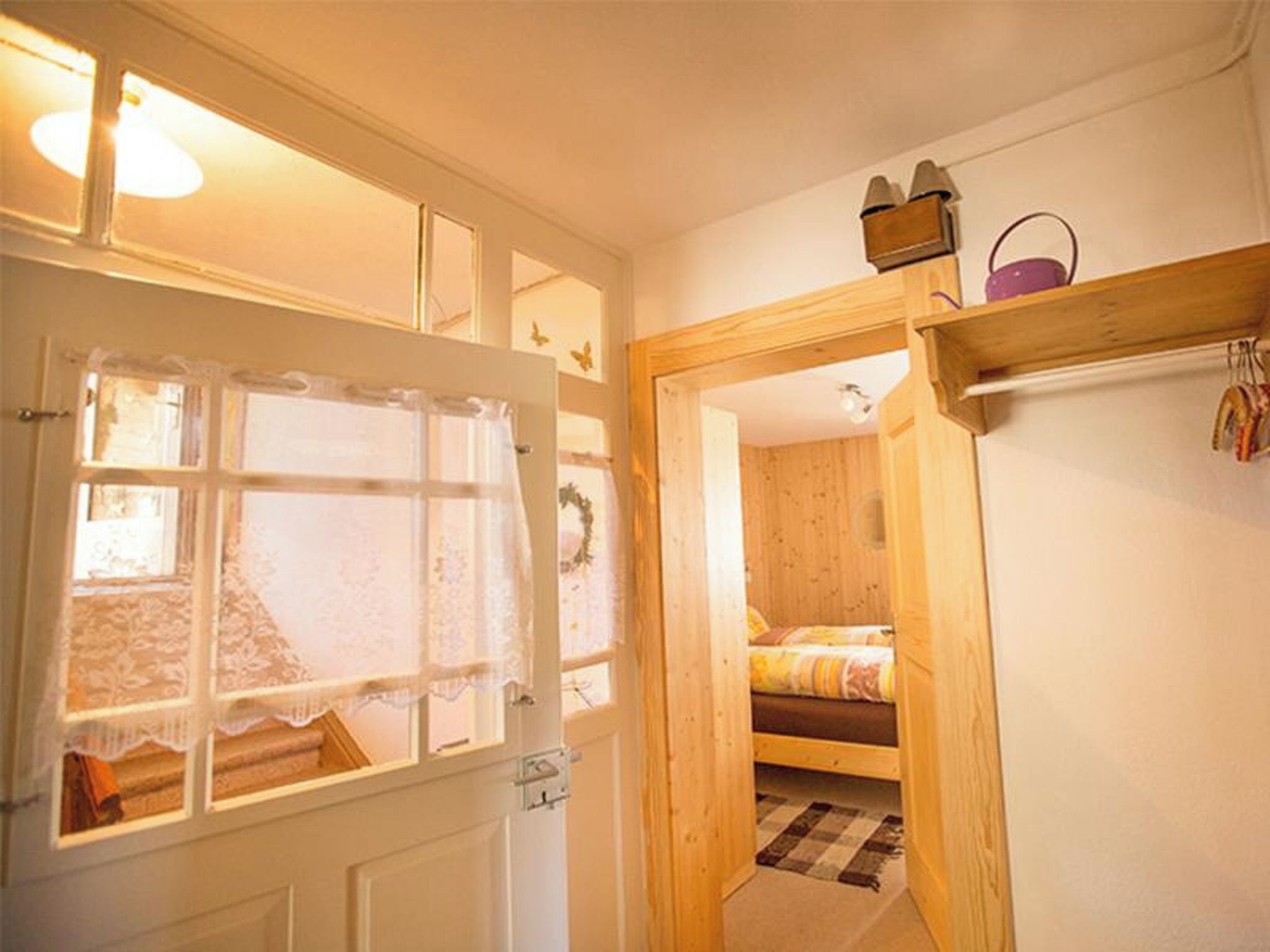 Ein Zimmer mit einem Bett, einer Holztür und einem Fenster mit Spitzenvorhängen.