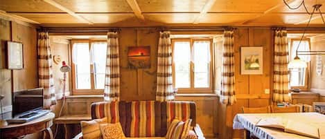Ein gemütliches Blockhaus-Interieur mit Holzbalkendecke, einer Couch mit gestreiften Kissen, einem Esstisch und einem Laptop auf einem Beistelltisch.