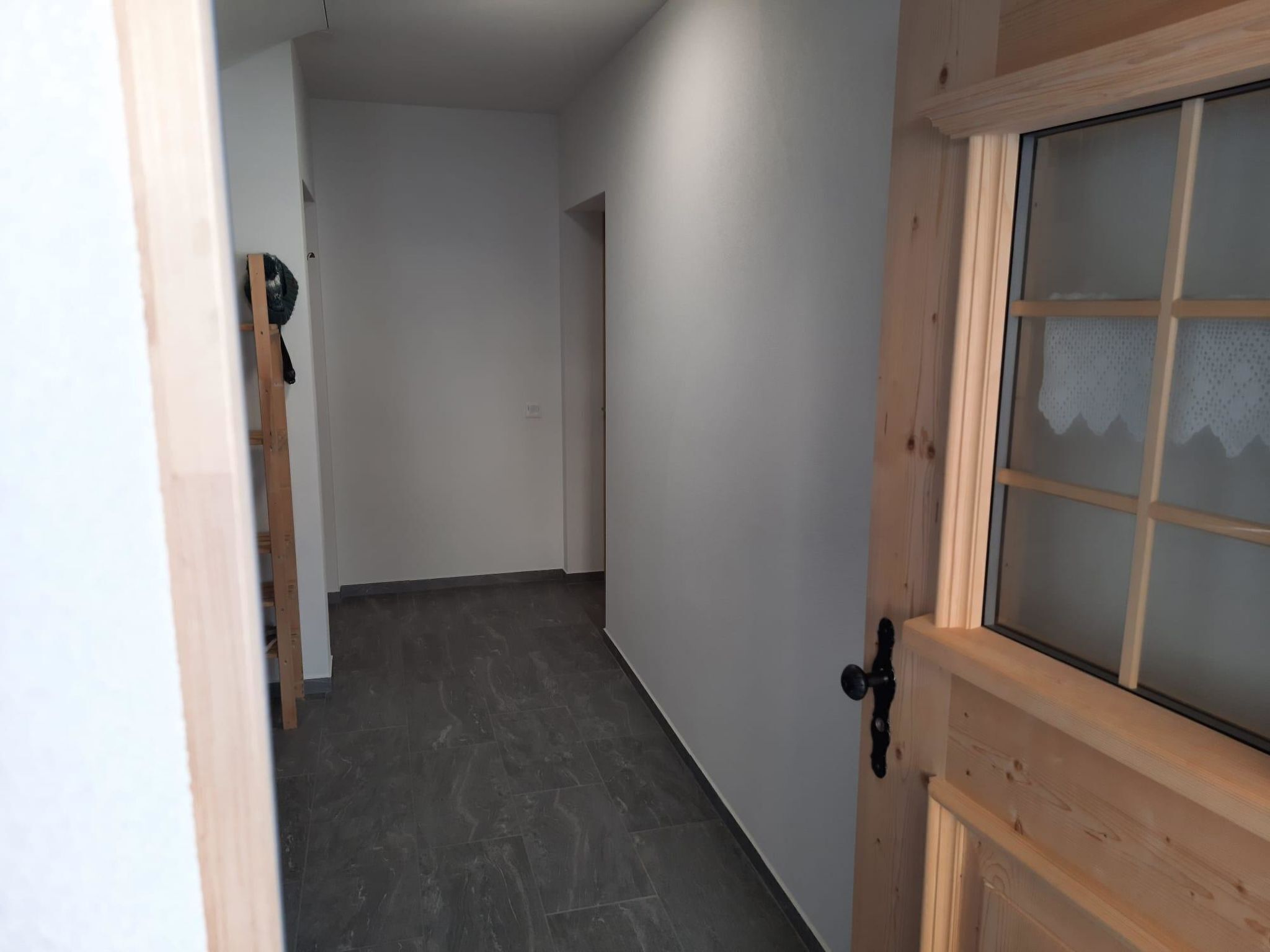 A hallway with a wooden door and a window, leading to a room with a tiled floor.