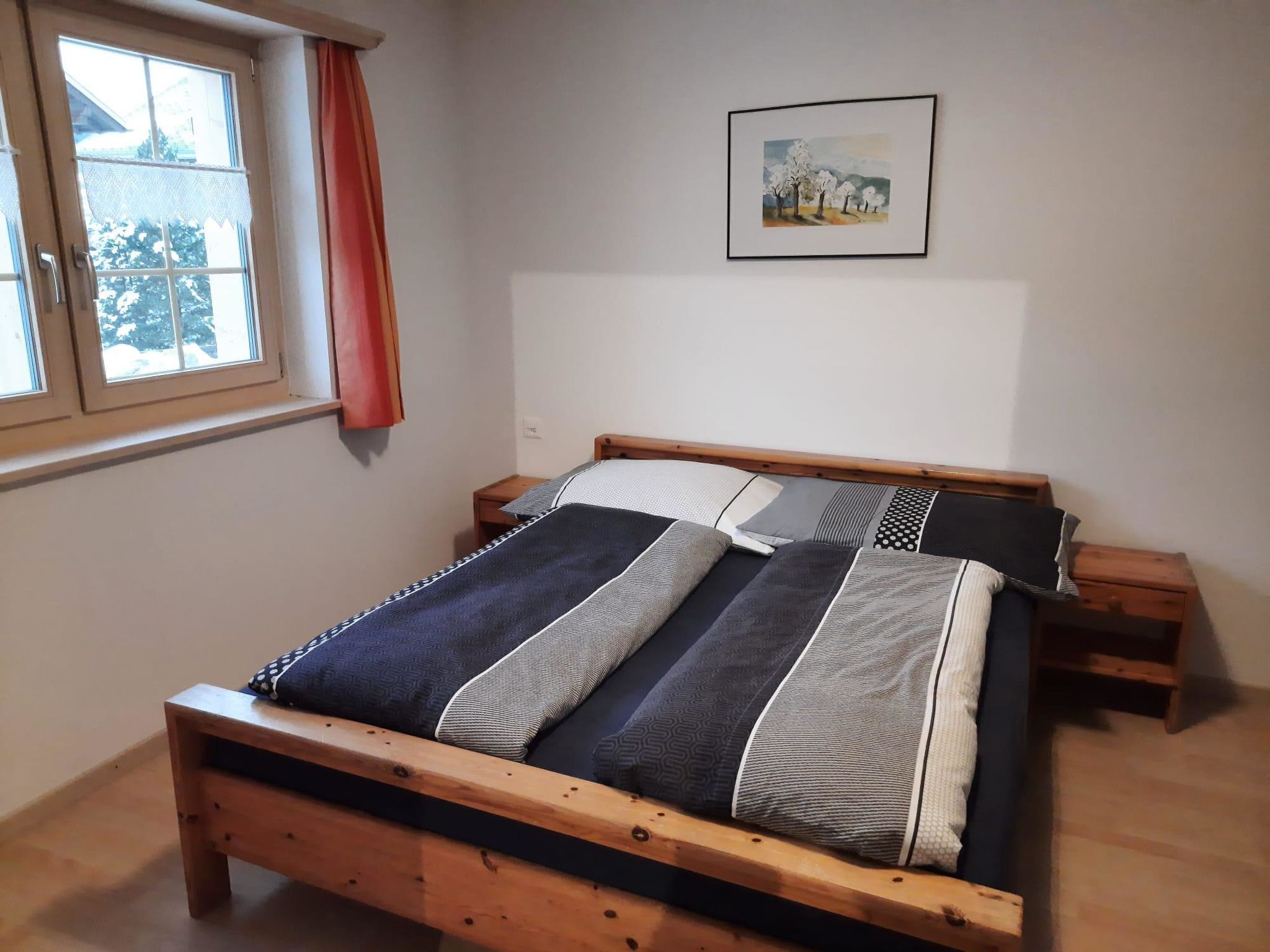 A bedroom with a wooden bed, a window with a view of trees, and a painting on the wall.
