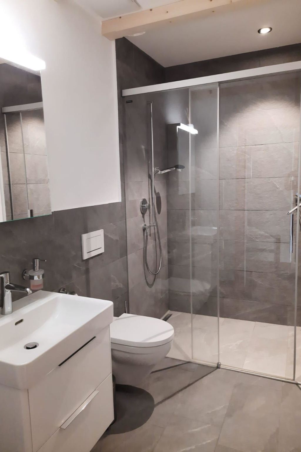 Een moderne badkamer met een douchecabine van glas, een witte wastafel en een toilet.