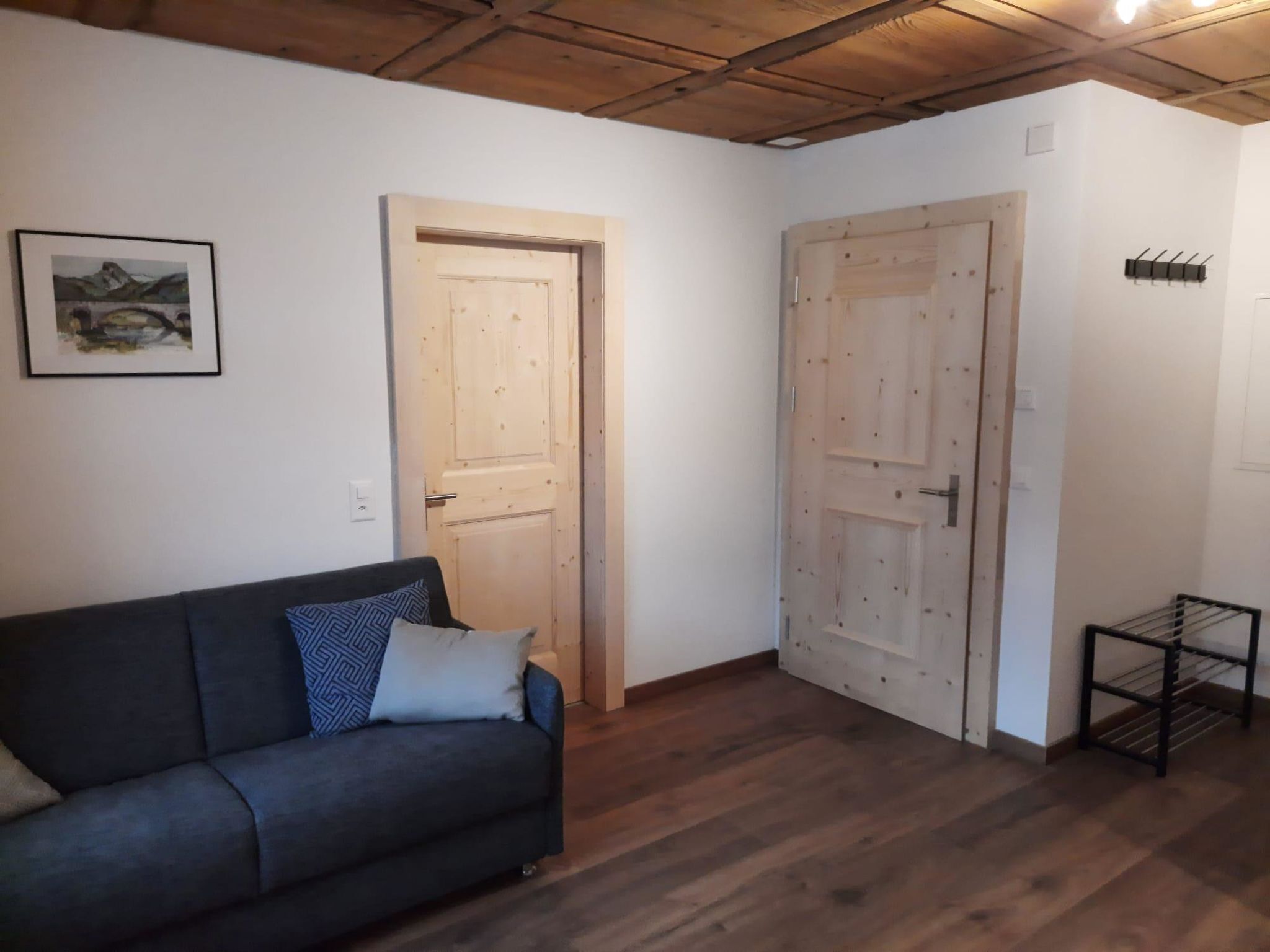 A room with a dark-colored sofa, two doors, a small metal rack, and a framed picture on the wall.