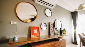 Un baño moderno con un tocador de vidrio, varios espejos, un cuadro enmarcado y un aire acondicionado de pared.