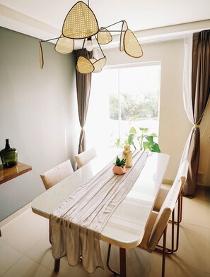 Uma sala de jantar com uma mesa comprida, cadeiras, um lustre e uma janela com cortinas.