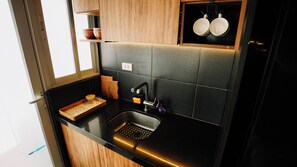 Una cocina compacta con encimera negra, pileta de acero inoxidable y una ventana sobre la pileta.
