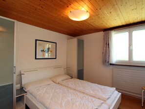 Ein Schlafzimmer mit einem Doppelbett, einem Nachttisch, einem gerahmten abstrakten Kunstwerk, einem Fenster mit Vorhängen und einer Holzbalkendecke.