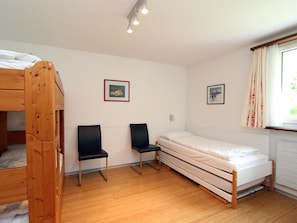 Une pièce comprenant un lit superposé, deux chaises, un lit simple et deux tableaux encadrés accrochés au mur.