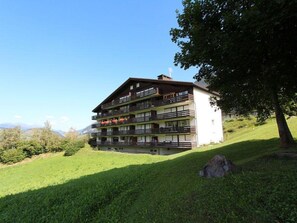 Ein mehrstöckiges Gebäude mit Balkonen, gelegen auf einem grasbewachsenen Hügel unter blauem Himmel.