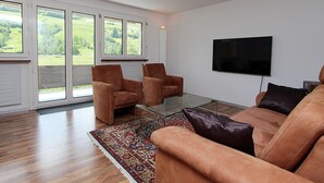 Una sala de estar moderna con un sofá, dos sillones, una mesa de centro y un televisor de pantalla plana montado en la pared.