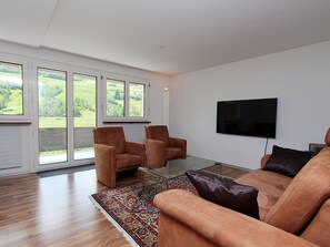 Ein modernes Wohnzimmer mit einer Couch, zwei Sesseln, einem Couchtisch und einem an der Wand montierten Flachbildfernseher.