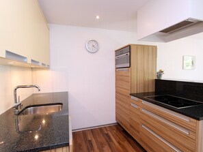 A modern kitchen with a granite countertop, stainless steel sink, wooden cabinets, and a black stovetop. - Las Vals D15 Appartement/Fewo, Bad, WC, 2 Schlafräume 3 Zimmerwohnung - 5 Betten by Interhome (Savognin)