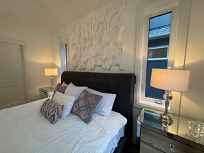 A hotel room with a large bed, two bedside lamps, a decorative wall piece, and a window with blinds.
