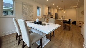 A modern kitchen with white cabinets, a dining area with a white table and chairs, and a wooden floor.