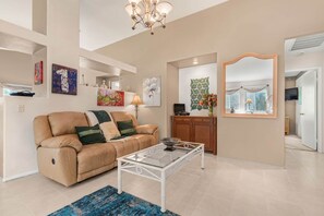 A living room with a beige sofa, a glass coffee table, and artwork on the walls.