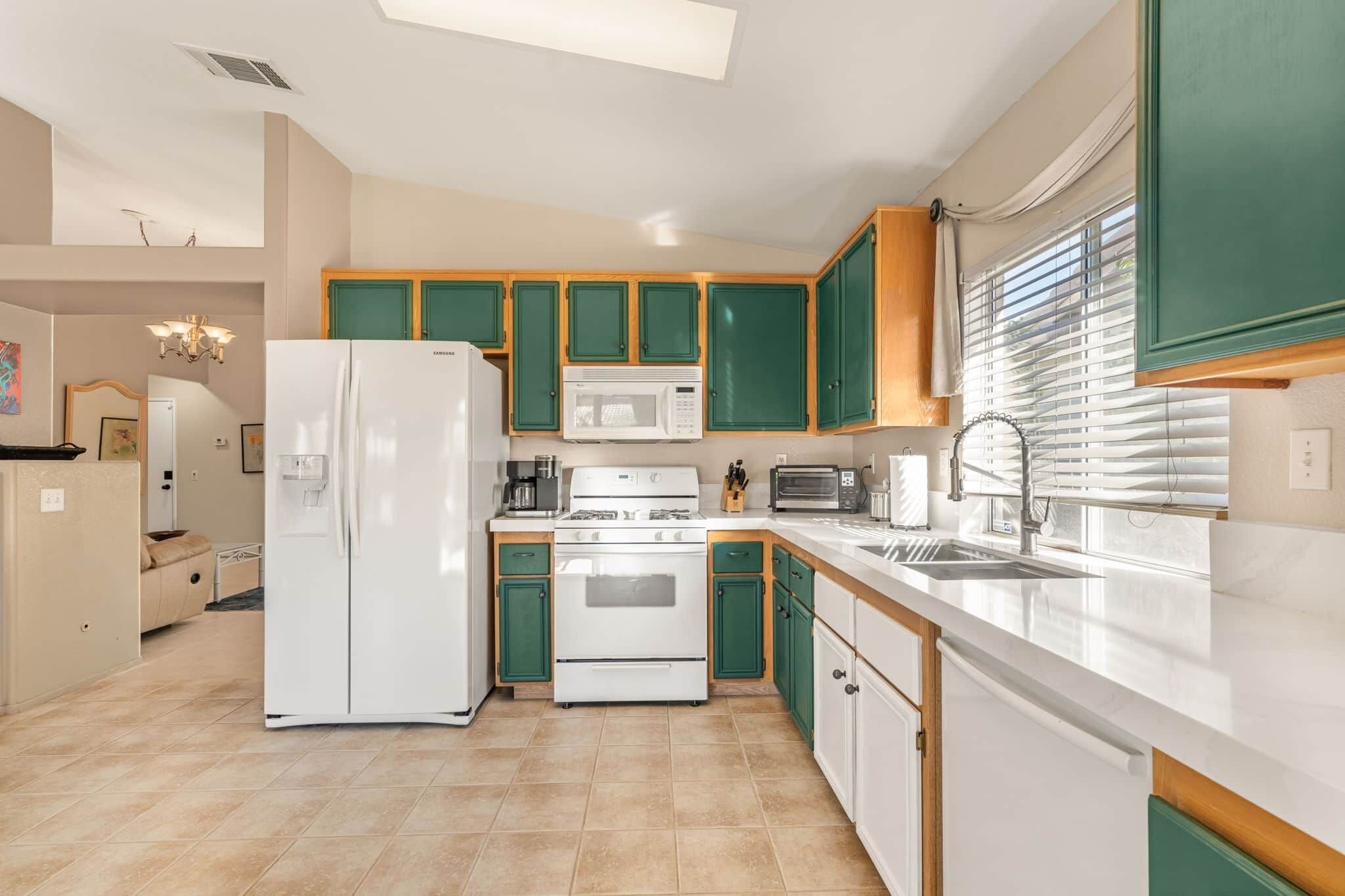Une cuisine avec des meubles de couleur verte, un réfrigérateur blanc, un four à micro-ondes, une cuisinière et un évier.