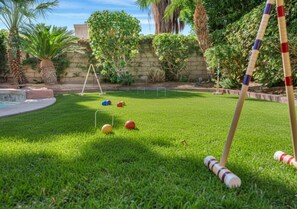 A well-maintained lawn with a croquet set, a small pool, and a stone wall with greenery.