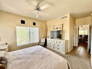 Une chambre à coucher avec un lit, une commode, un téléviseur et un ventilateur de plafond.