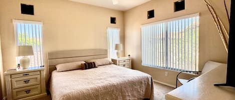 A bedroom with a bed, bedside tables, a ceiling fan, and windows with blinds.