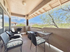 An outdoor patio with wicker furniture, a table, and a view of a mountainous landscape. - Vistoso Condo #216A (Oro Valley)