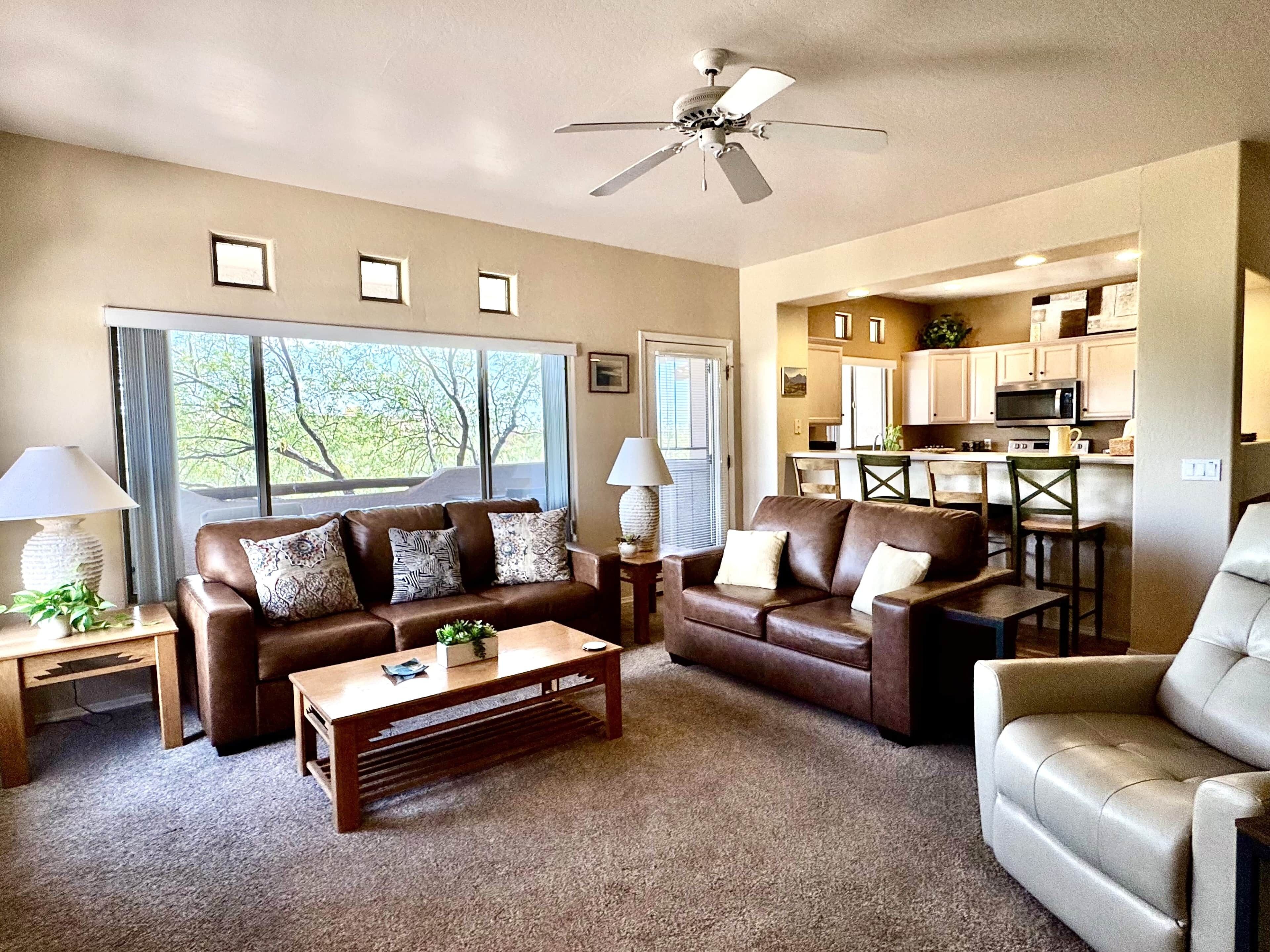 A living room with a brown leather sofa, a wooden coffee table, and a ceiling fan.