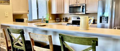 A kitchen with a central island, bar stools, a microwave, oven, refrigerator, and a sink.