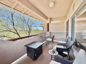 Ein Balkon mit Tisch und Stühlen, ein kleiner Tisch mit einer Pflanze und Blick auf Bäume sowie ein Gebäude in der Ferne.