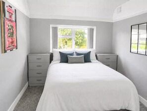 A bedroom with a bed, two bedside tables, a window, and a wall-mounted artwork. - Vivian - Luxury 2 bed House (Watford)