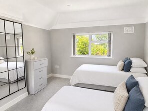 A bedroom with two beds, a dresser, a mirror, and a window with a view of greenery. - Vivian - Luxury 2 bed House (Watford)