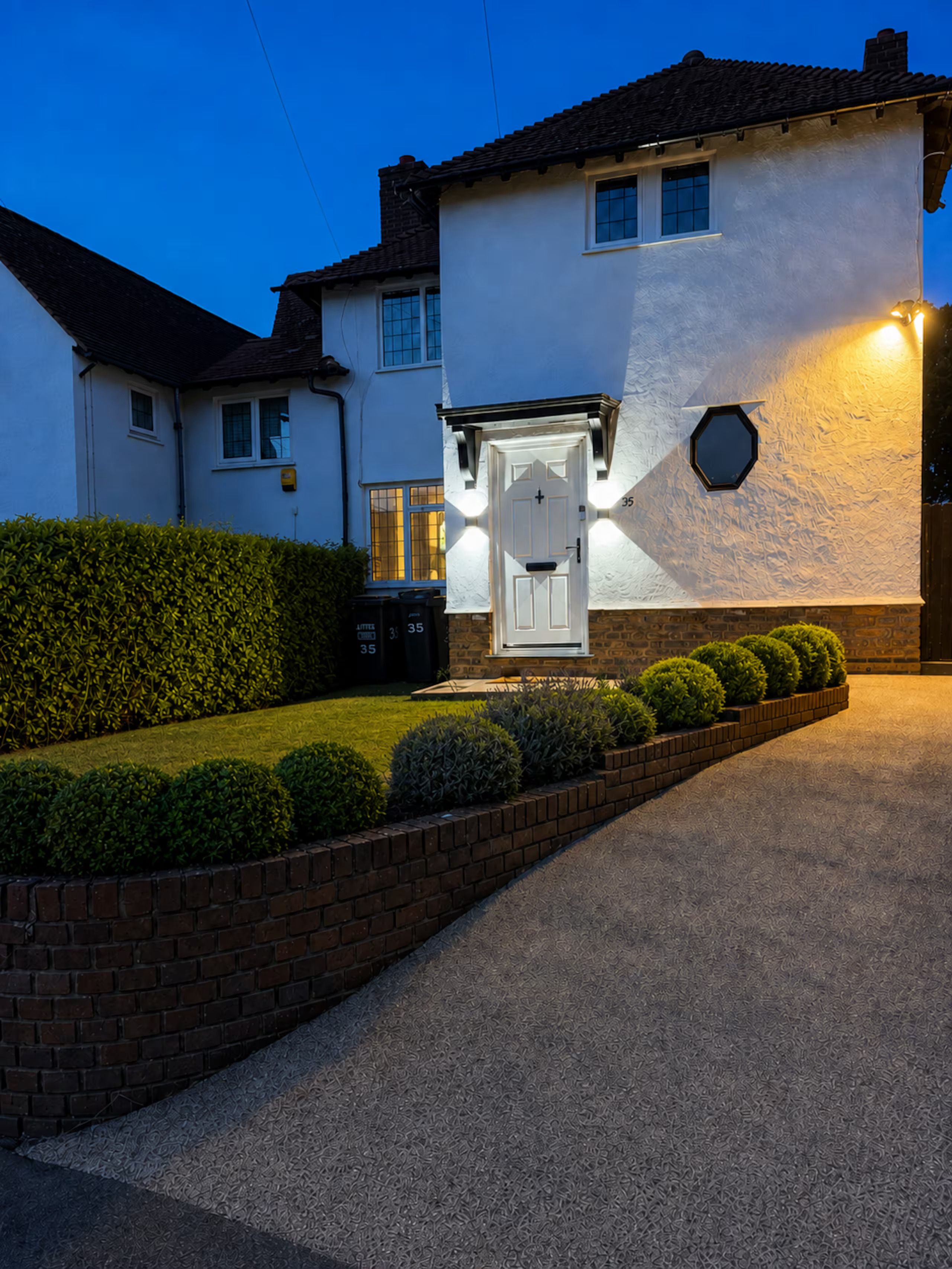 A two-story house with a white exterior, a brick driveway, and a well-maintained front yard with hedges.