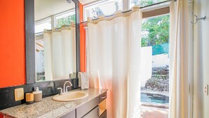 A bathroom with a sink, mirror, and a view of a garden through a glass door. - Waves Sunzal (Tamanique)