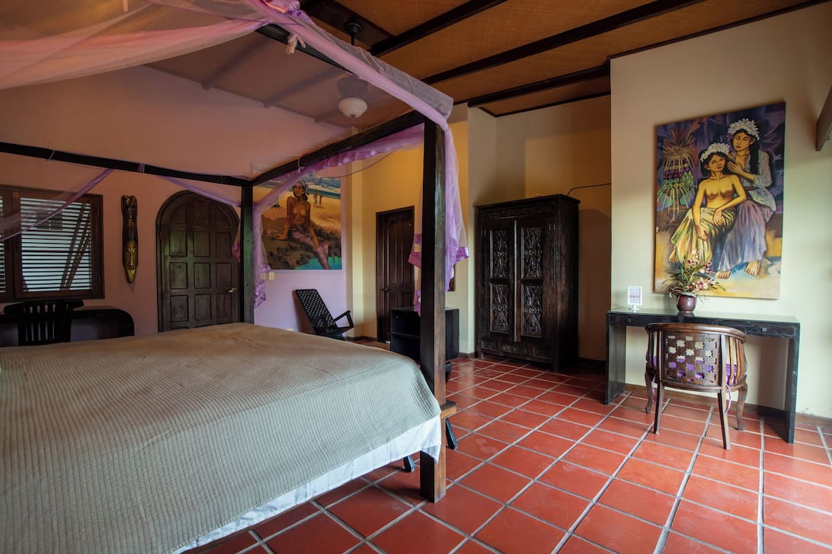 A bedroom with a bed, a chair, a desk, and a painting on the wall.
