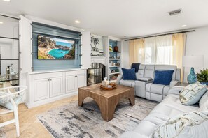 Ein Wohnzimmer mit Fernseher, weißen Möbeln, einem Couchtisch und einem Bücherregal.