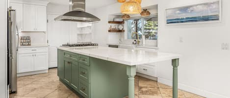 A modern kitchen with a central island, white cabinetry, a stainless steel range hood, and a hanging light fixture.