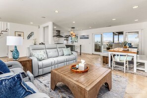 A spacious living area with a grey sofa, wooden coffee table, and a dining table with chairs. - Del Mar Coastal Luxury: Minutes to Beach & Trails (Del Mar)