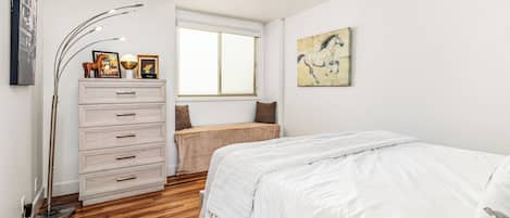 A bedroom with a bed, a dresser, a window, and a painting on the wall.