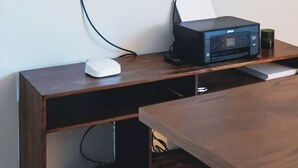 Een flatscreen televisie bevestigd aan een muur boven een houten bureau met een printer en een muis.