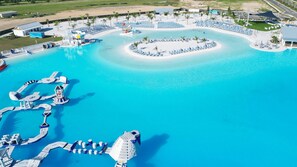 Eine Vogelperspektive zeigt einen Resortkomplex mit einem großen zentralen Pool, mehreren kleineren Pools sowie verschiedenen Wasserrutschen und Spielgeräten.