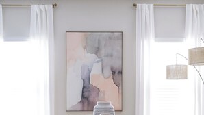 Een moderne eetruimte met een ronde tafel, gestoffeerde grijze stoelen en een groot abstract schilderij aan de muur.