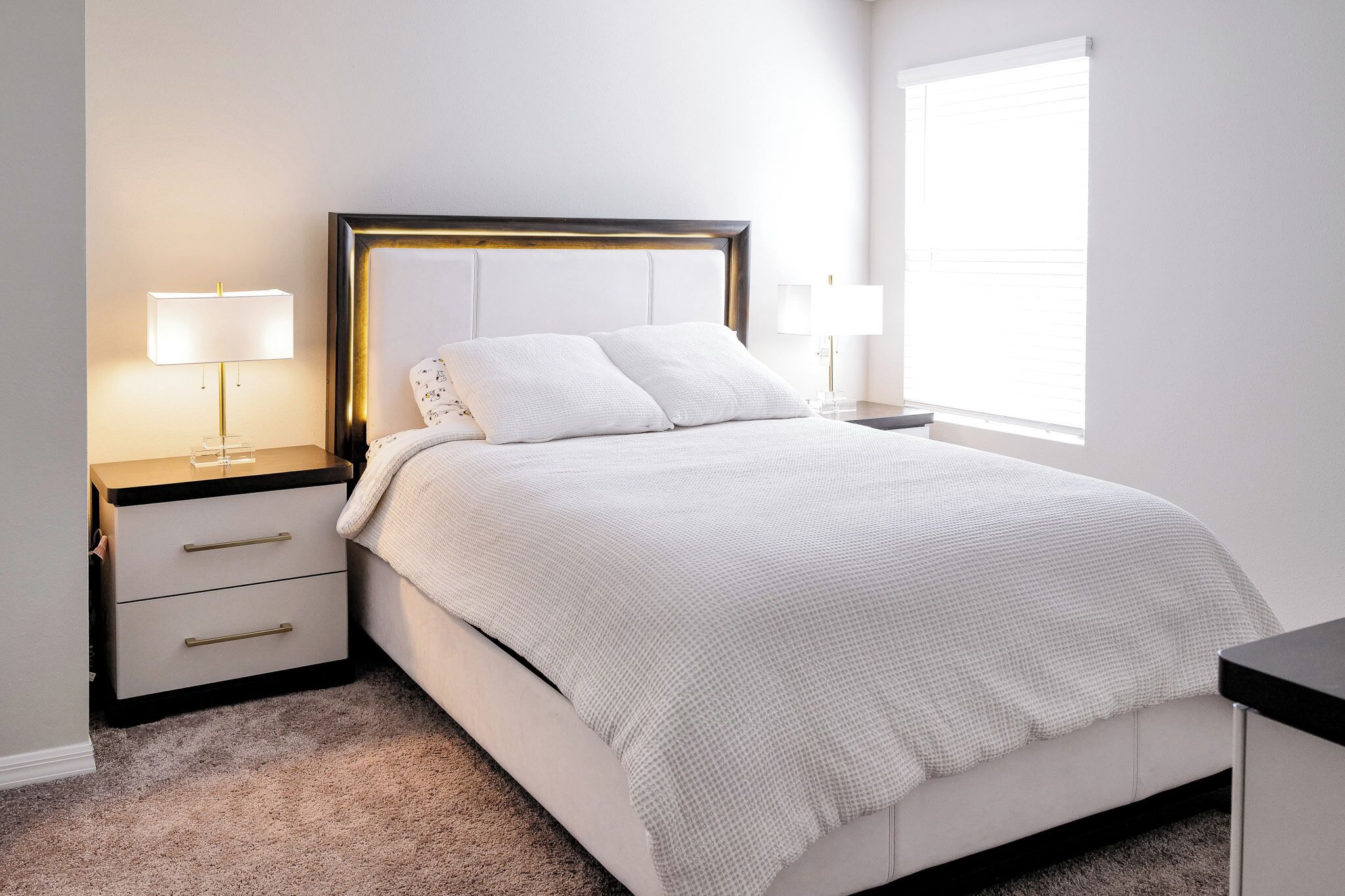 Un dormitorio con cama, mesitas de noche, lámparas y una ventana.