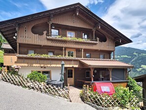 Ein mehrstöckiges Holzchalet mit Balkonen, einer überdachten Terrasse und Blick auf die umliegende Landschaft.