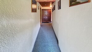 Um corredor com teto de madeira, paredes brancas e piso coberto de carpete. Há quadros nas paredes e uma porta no final.