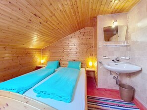 Ein Zimmer mit Holzbalkendecke, einem Bett mit blauer Bettwäsche, einem weißen Waschbecken und einem Spiegel.