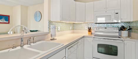A kitchen with white cabinets, a sink, a microwave, and an oven.