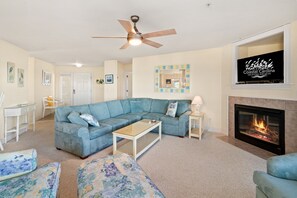 A living room with a sectional sofa, a coffee table, a fireplace, and a ceiling fan. - Ballast Point Villa 1411: Soundfront, Pirate's Cove Community Amenities, Water Views (Manteo)