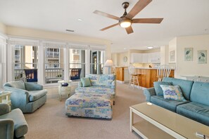 Ein geräumiges Wohnzimmer mit Deckenventilator, großen Fenstern, Küchenzeile und Esstisch.