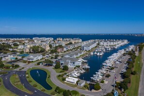 An aerial view of a marina with numerous boats docked, surrounded by residential buildings and a curved road. - Ballast Point Villa 1411: Soundfront, Pirate's Cove Community Amenities, Water Views (Manteo)