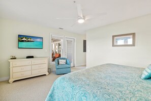 Ein Schlafzimmer mit Bett, Kommode, Stuhl, Deckenventilator und Fernseher.