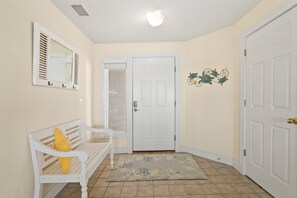 A hallway with a white bench, a door, and a wall-mounted mirror. - Ballast Point Villa 1411: Soundfront, Pirate's Cove Community Amenities, Water Views (Manteo)