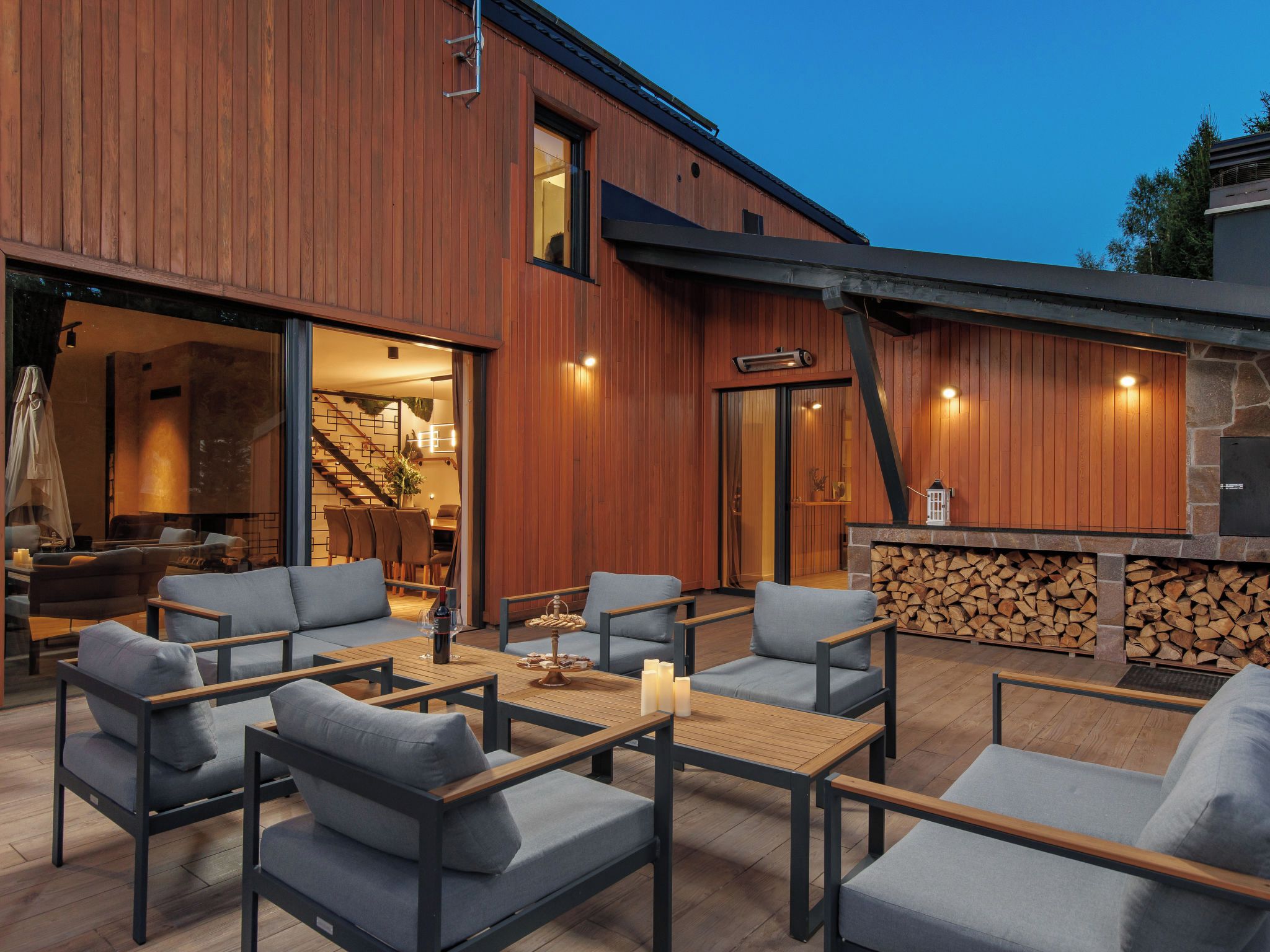 An outdoor seating area with sofas and tables, a stone fireplace, and a wooden exterior wall.