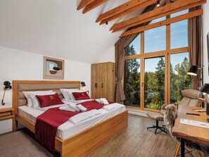 Een hotelkamer met een houten bed, een bureau met een stoel, een groot raam met uitzicht op bomen en een plafond met zichtbare balken.